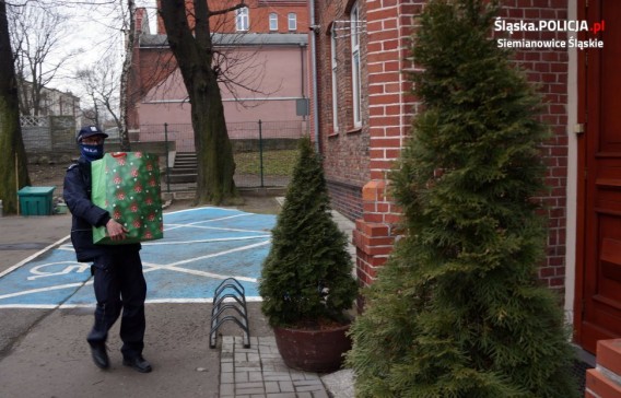 Policjant z paczką przed wejściem do budynku.