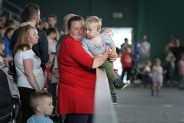 Na pierwszym planie kobieta z dzieckiem na rękach. W rozmytym tle publiczność i bawiące się dzieci