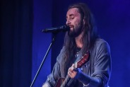 Zbliżenie na postać Łukasza Łyczkowskiego, wokalisty zespołu 5 Rano. Gra na gitarze i śpiewa do…