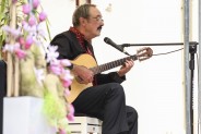 Aleksandr Maceradi siedzi na scenie, gra na gitarze i śpiewa. Bliskie ujęcie z prawego profilu, w…