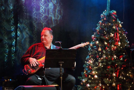Basista Andrzej Rusek siedzący z gitarą na scenie SCK- Bytków. Obok choinka