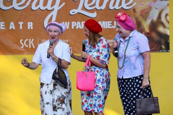 Trzy aktorki ubrane i umalowane w sposób krzykliwy i kolorowy stoją na scenie amfiteatru i mówią…