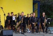 Na scenie amfiteatru muzycy orkiestry Siemion Band. Siedzą na krzesłach ubrani na czarno i grają…
