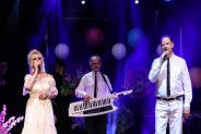 Na scenie SCK troje artystów z zespołu Duet Karo. Wszyscy ubrani na biało. Kobieta w długiej…