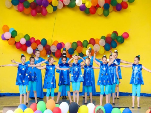 Na żółtym tle sceny amfiteatru wiszą kolorowe balony. Na scenie występuje dziecięcy zespół…