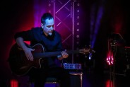 Na scenie siedzi gitarzysta zespołu Mikromusic i gra na gitarze. Za nim kolorowe światła…